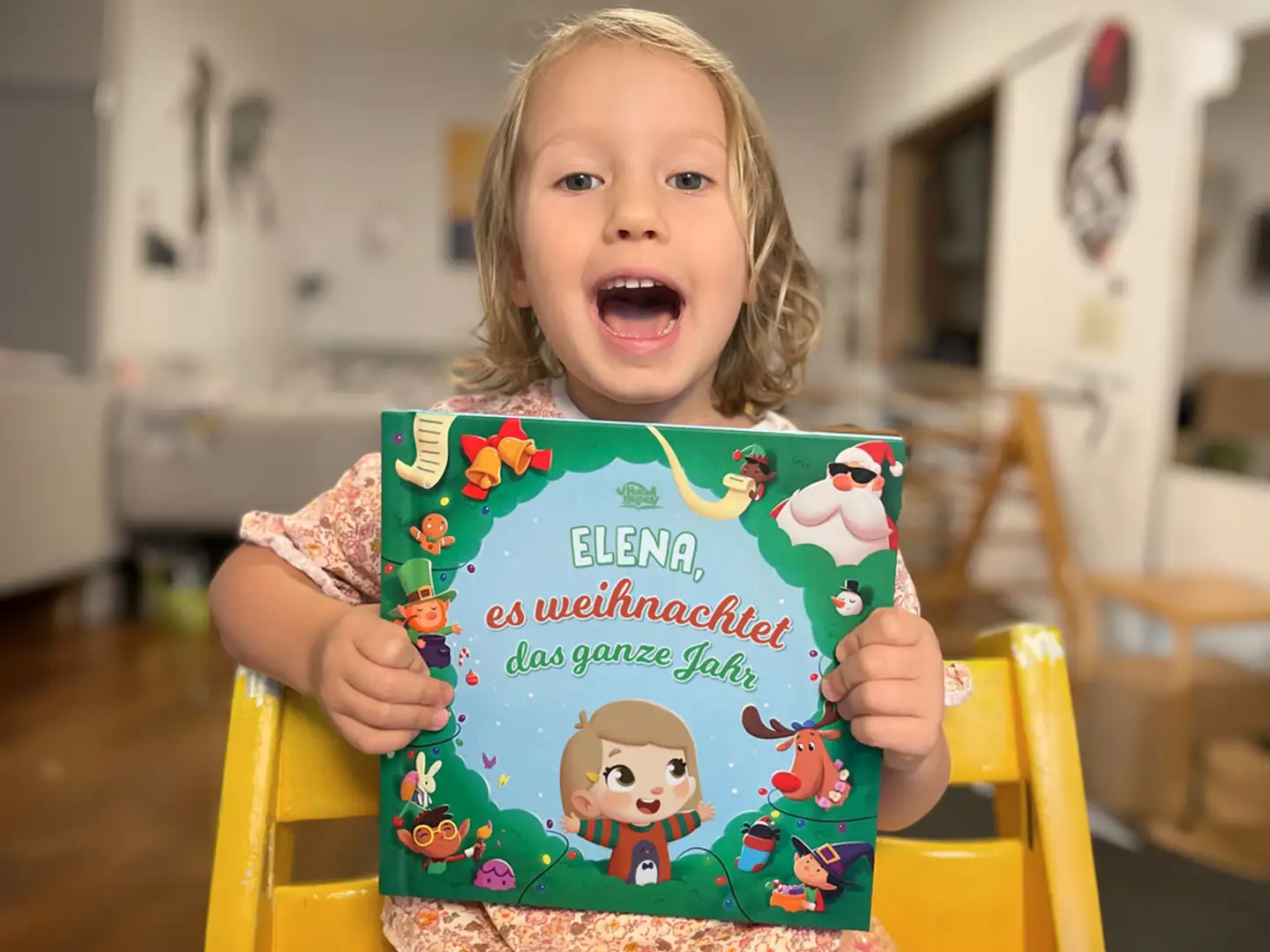 Kleines Mädchen lächelt und hält ihr personalisiertes Buch über Weihnachten in den Händen.